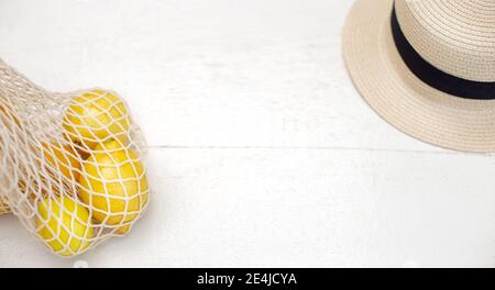 Sur une table en bois blanc, à côté se trouve un sac tricoté avec des citrons et un chapeau de paille. Banque D'Images
