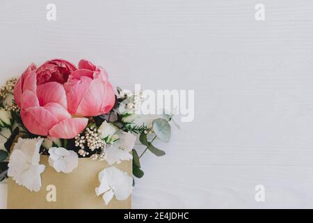 Pivoine, fleurs blanches et eucalyptus provenant d'une enveloppe artisanale sur bois blanc, plat avec espace pour le texte. Carte de vœux ou envoi à motif fleuri créatif Banque D'Images