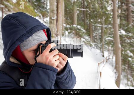 Homme photographe avec appareil photo prend des photos de paysage de forêt d'hiver. Banque D'Images