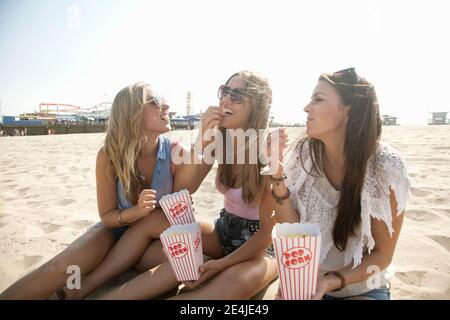 Des amis souriants mangent du pop-corn à la plage par beau temps Banque D'Images