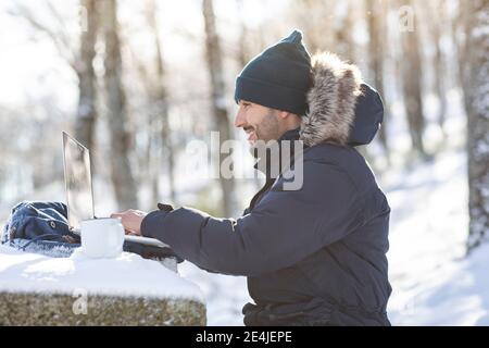 Homme d'affaires souriant travaillant sur un ordinateur portable sous la neige Banque D'Images