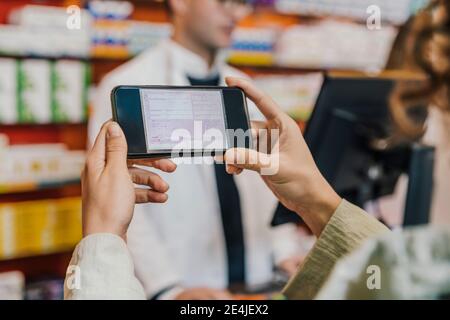 Main du client utilisant un téléphone intelligent pour la prescription dans un pharmacien stocker Banque D'Images