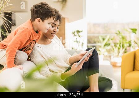 Femme montrant une tablette numérique à un garçon tout en étant assise à la maison Banque D'Images