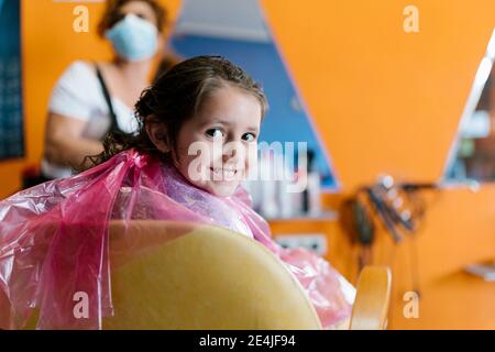 Souriante petite fille portant un tablier rose avec coiffeur à barber boutique Banque D'Images