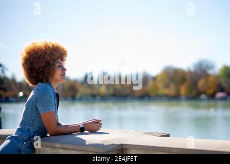 Femme souriante contemplant tout en s'inclinant sur la rampe en face de l'étang de l'Estanque Grande Del Retiro, Espagne Banque D'Images