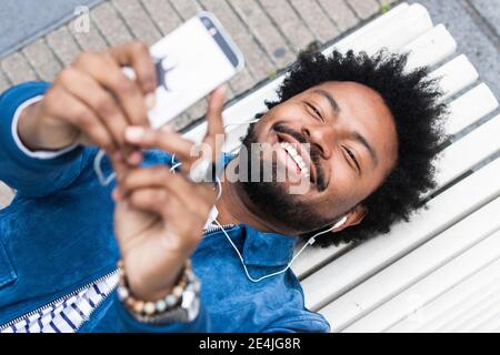 Gros plan de l'homme gai avec la musique d'écoute de cheveux afro et utilisation d'un téléphone portable en étant allongé sur une paillasse Banque D'Images