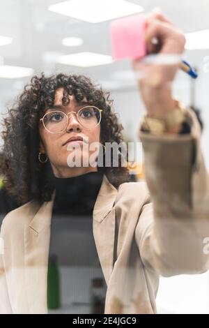 Une jeune femme d'affaires écrit de nouvelles idées sur des notes adhésives au bureau Banque D'Images