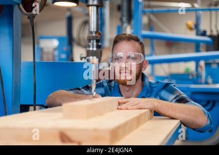 Portrait de menuisier portant des lunettes de protection, perçant une planche en bois Banque D'Images