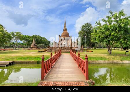 Pont en bois rouge traversant l'étang menant à la pagode et au complexe de monastère de chapelle en ruines au temple Wat sa si, Parc historique de Sukhothai, Thaïlande Banque D'Images