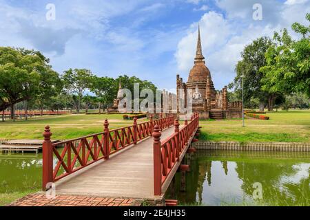 Pont en bois rouge traversant l'étang menant à la pagode et au complexe de monastère de chapelle en ruines au temple Wat sa si, Parc historique de Sukhothai, Thaïlande Banque D'Images