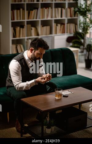 Homme barbu assis sur un canapé préparant une pipe à fumer Banque D'Images