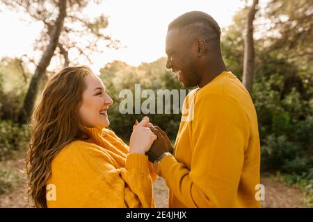 Couple heureux tenant les mains en se tenant debout en forêt Banque D'Images