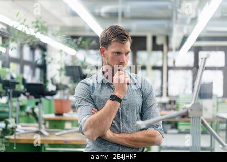 Homme professionnel à la main sur le menton regardant le modèle de moulin à vent lors du travail en usine Banque D'Images