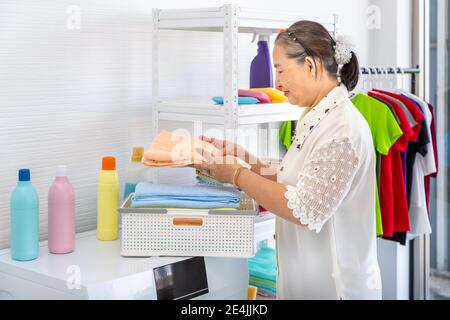 Happy souriant asiatique senior femme femme pliante vêtements de blanchisserie avec machine à laver, nettoyage de maison et concept de ménage Banque D'Images