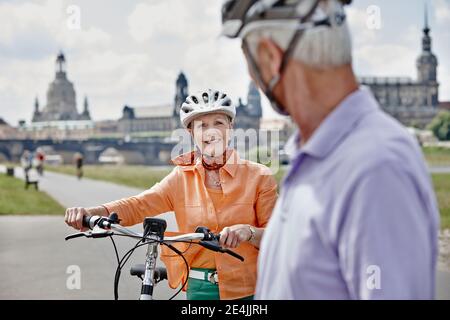 Femme âgée avec vélo électrique souriant tout en regardant l'homme en se tenant à la cathédrale Frauenkirche, Dresde, Allemagne Banque D'Images