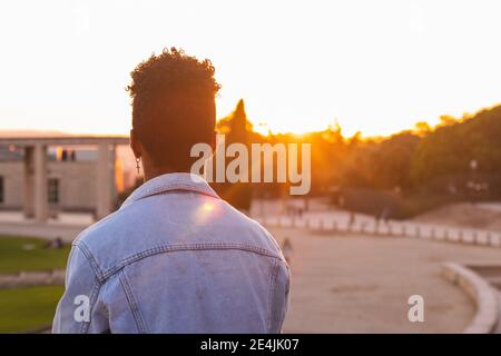 Jeune homme portant une veste en denim debout au parc au coucher du soleil Banque D'Images