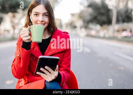 Jeune femme à la mode prenant un café tout en tenant une tablette numérique rue Banque D'Images