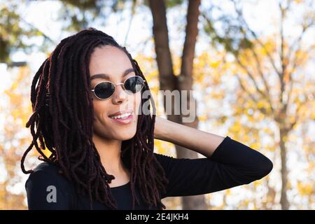 Jeune femme à la mode avec des dreadlocks portant des lunettes de soleil au parc Banque D'Images