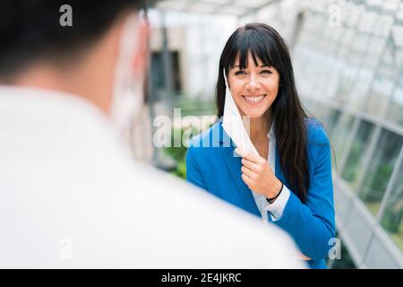 Femme entrepreneure souriante regardant un collègue pendant une réunion de bureau tout en tenant le masque Banque D'Images