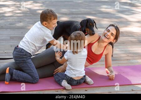 Jeune belle mère avec bébé fils, fille et avec chien faisant de l'exercice et faisant du yoga au parc d'été au lever du soleil. La maternité sportive et saine. Fern
