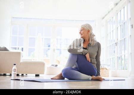 Femme âgée qui fait de l'exercice tout en regardant loin à la maison Banque D'Images