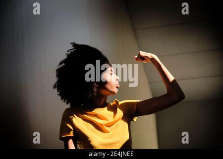 Jeune femme montrant des muscles en se tenant contre le mur Banque D'Images