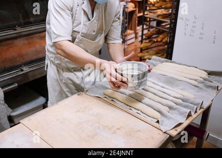 Chef cuisinier masculin tamisant la farine du tamis sur la pâte dans la boulangerie Banque D'Images