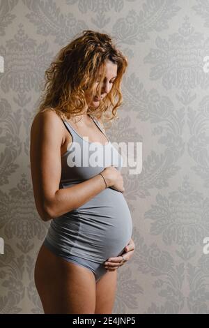 Jeune enceinte touchant l'abdomen contre le mur à la maison Banque D'Images