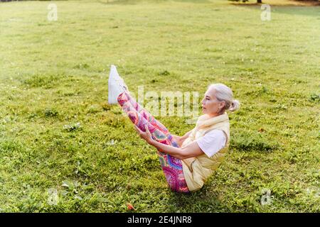 Femme mature pratiquant le yoga sur l'herbe dans le parc public Banque D'Images