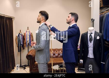 Tailleur dans son magasin de vêtements pour hommes prenant des mesures de clients pour la tenue Banque D'Images