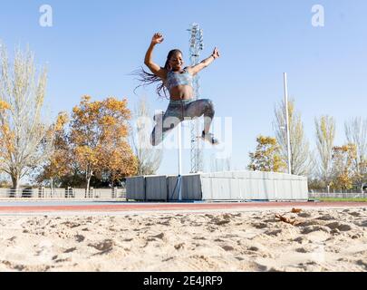 Entraînement sportif joyeux pour un long saut sur le sable au soleil jour Banque D'Images