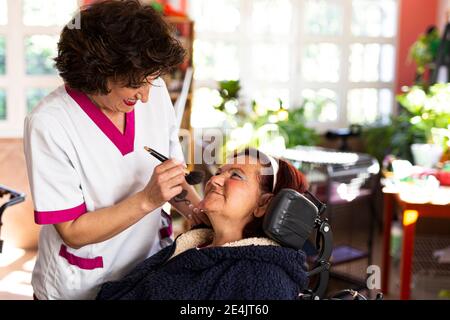 Femme souriante qui fait le maquillage de la femme handicapée en soins infirmiers accueil Banque D'Images