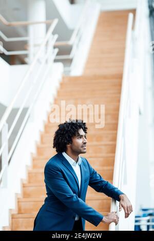 Homme d'affaires attentionné se penchait sur les balustrades d'escalier tout en regardant loin bureau Banque D'Images