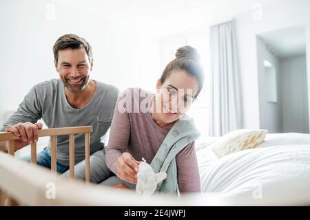 Homme et femme mûrs souriants avec jouet éléphant bourré jouant par lit de bébé dans la chambre Banque D'Images