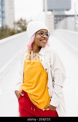 Femme portant un chapeau et une perruque en regardant loin tout en étant debout avec mains dans les poches sur le pont Banque D'Images