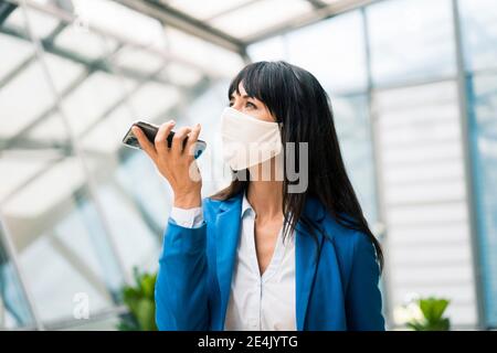 Femme d'affaires envoyant la messagerie vocale par téléphone intelligent au bureau pendant COVID-19 Banque D'Images