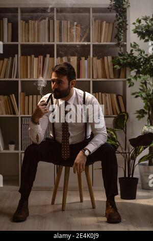 Portrait d'un homme barbu assis sur un tabouret et un tuyau de fumée Banque D'Images