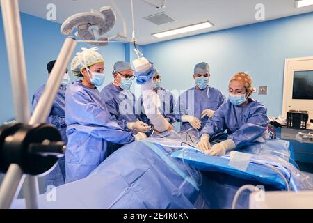 Les médecins portant un masque facial faisant une chirurgie arthroscopique du patient pendant debout près de la table dans la salle d'opération pendant la COVID-19 Banque D'Images