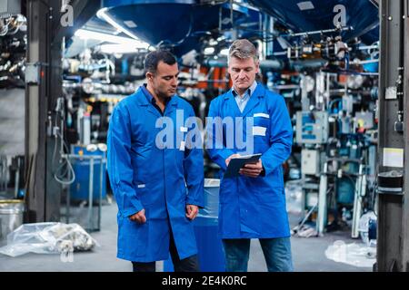 Les techniciens masculins sont en couche bleue et utilisent une tablette numérique pendant leur travail dans l'industrie Banque D'Images