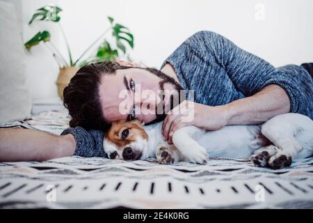 Jeune homme allongé avec un chien sur le lit à la maison Banque D'Images