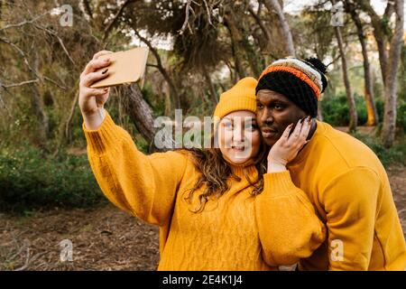 Jeune femme portant un chapeau tricoté et portant un selfie sur un téléphone portable en forêt Banque D'Images