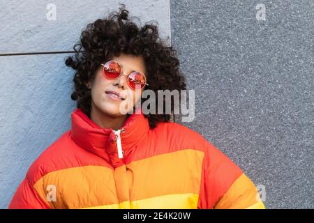 Jeune femme portant des lunettes de soleil souriant tout en se penchant sur le mur Banque D'Images