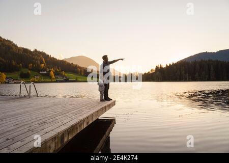 Père et petite fille debout ensemble au bord du lac jetée au coucher du soleil Banque D'Images