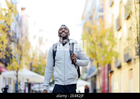 Jeune homme avec sac à dos souriant en marchant en ville Banque D'Images