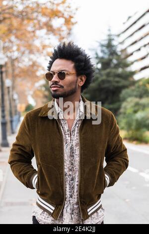 Homme moyen et élégant portant des lunettes de soleil avec les mains dans les poches debout dans la rue Banque D'Images