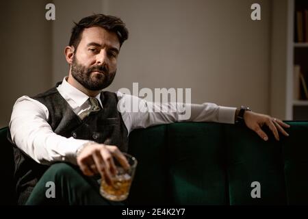 Portrait de l'homme barbu assis sur un canapé avec un verre de chuchoter à la main Banque D'Images