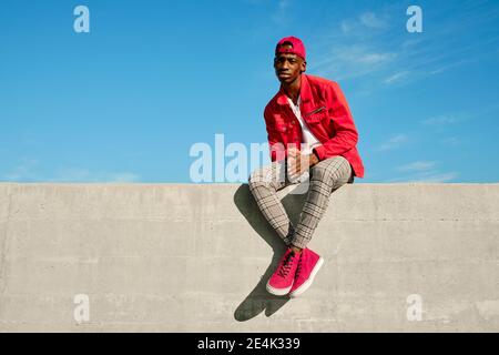 Jeune homme en veste rouge et casquette de baseball mur en béton Banque D'Images