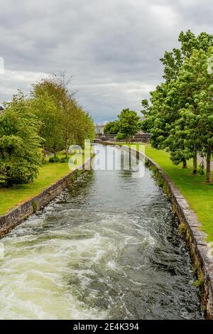 Middle River avec l'eau qui coule vers Bridge Street au milieu de l'herbe et des arbres avec le feuillage vert, les voies d'eau de Galway, jour nuageux à Galway City, Conn Banque D'Images