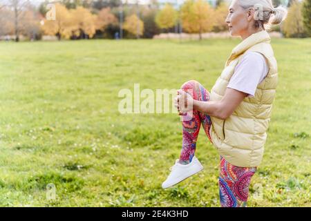 Femme mûre s'étirant sur une jambe au-dessus de l'herbe au parc public Banque D'Images