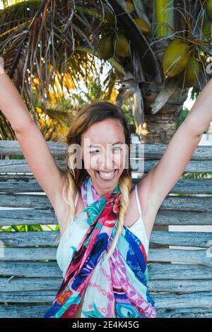 Joyeuse femme paix gestante avec les armes soulevées contre la clôture en bois à la plage Banque D'Images